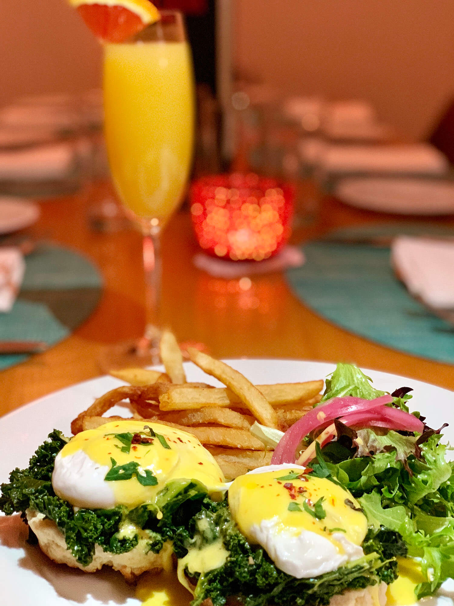Eggs Benedict with hollandaise sauce over sautéed kale, served with French fries and mixed greens salad with pickled onions.
