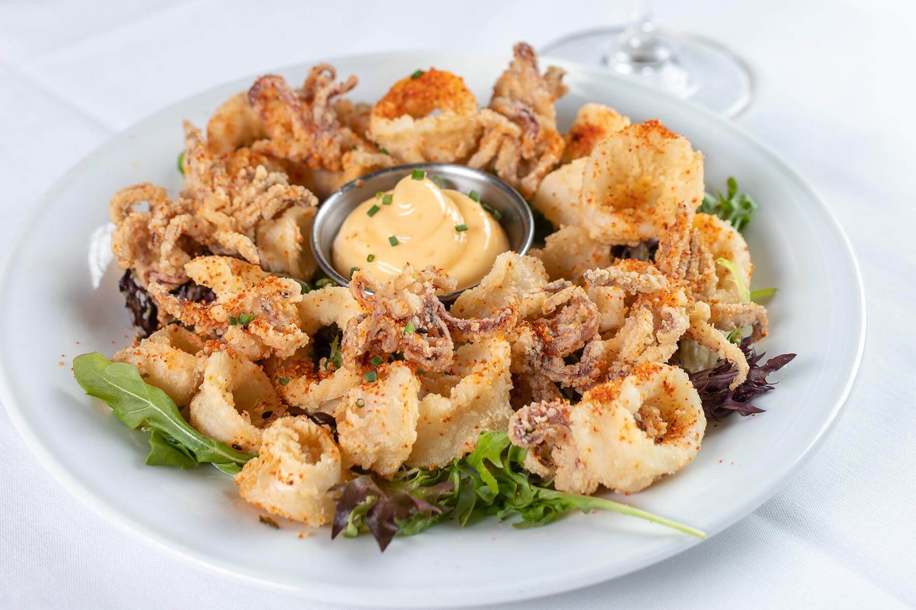 Plate of fried calamari garnished with herbs and served with a side of creamy dipping sauce.