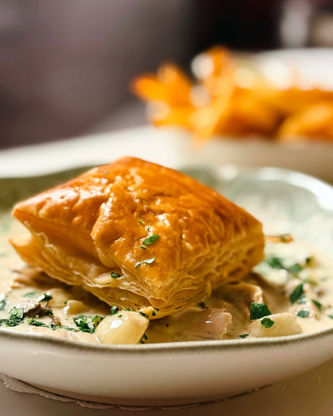 Golden-brown puff pastry square served on a creamy sauce with herbs, garnished with chopped parsley.